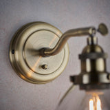 Wentworth Wall Light in brass, close-up of the round wall plate, adjustable knuckle joint and knurled lamp holder with glass shade against a light background.