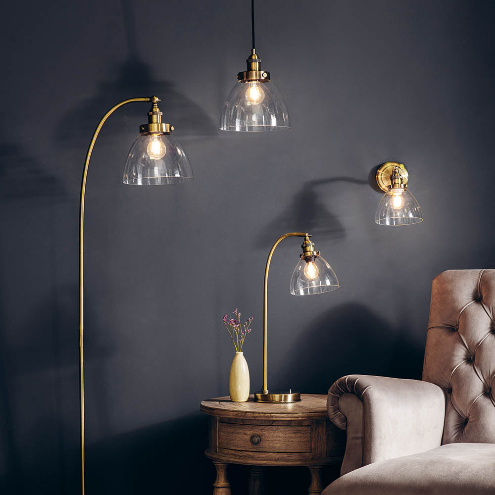 Wentworth Table Lamp in brass with clear glass dome shade and adjustable arm, shown lit on a side table beside matching pendant and wall lights.