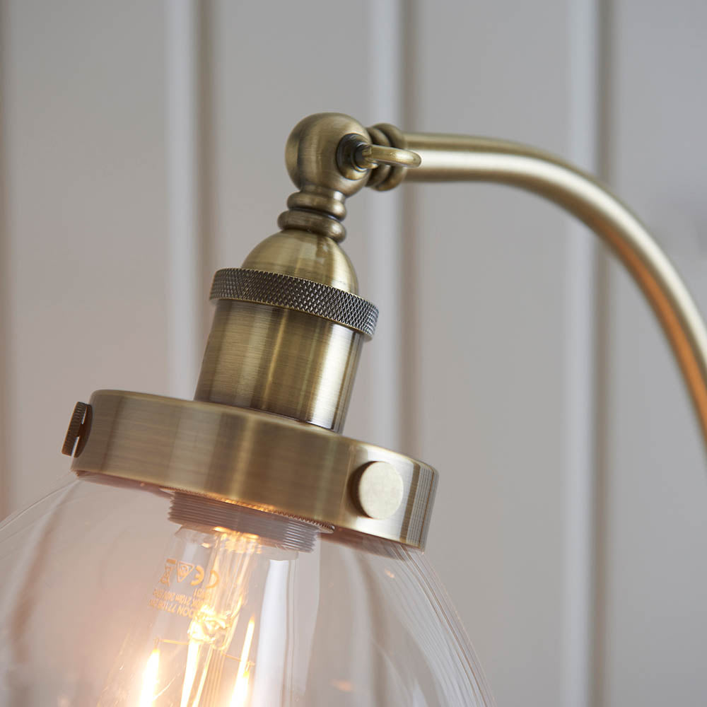Close-up of the Endon Wentworth Floor Lamp in antique brass, showing the knurled lamp holder, adjustable knuckle, and clear glass shade with E27 bulb.