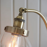 Close-up of the Endon Wentworth Floor Lamp in antique brass, showing the knurled lamp holder, adjustable knuckle, and clear glass shade with E27 bulb.