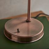 Close-up of the copper base and toggle switch on Endon's Wentworth industrial table lamp, resting on a green surface with black fabric flex.