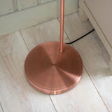Endon Wentworth floor lamp base in copper finish, showing the circular weighted base and stem on light wood plank flooring beside skirting.