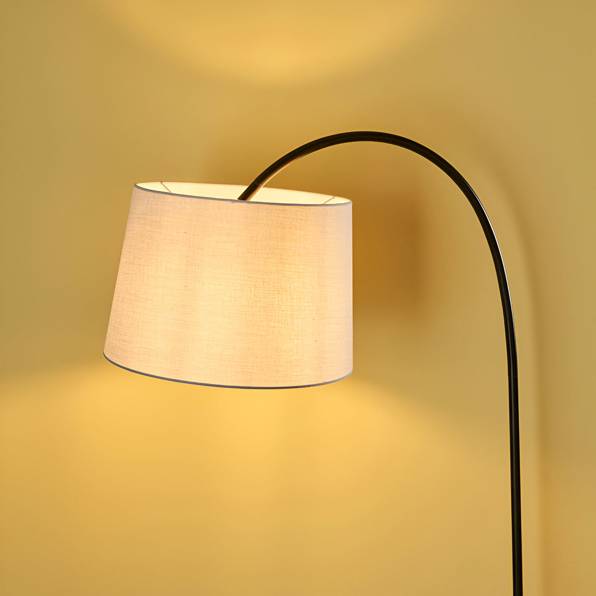 Endon Bevbourne arched floor lamp with matt black metal stem and tilted light grey fabric drum shade, illuminated against a warm neutral background.