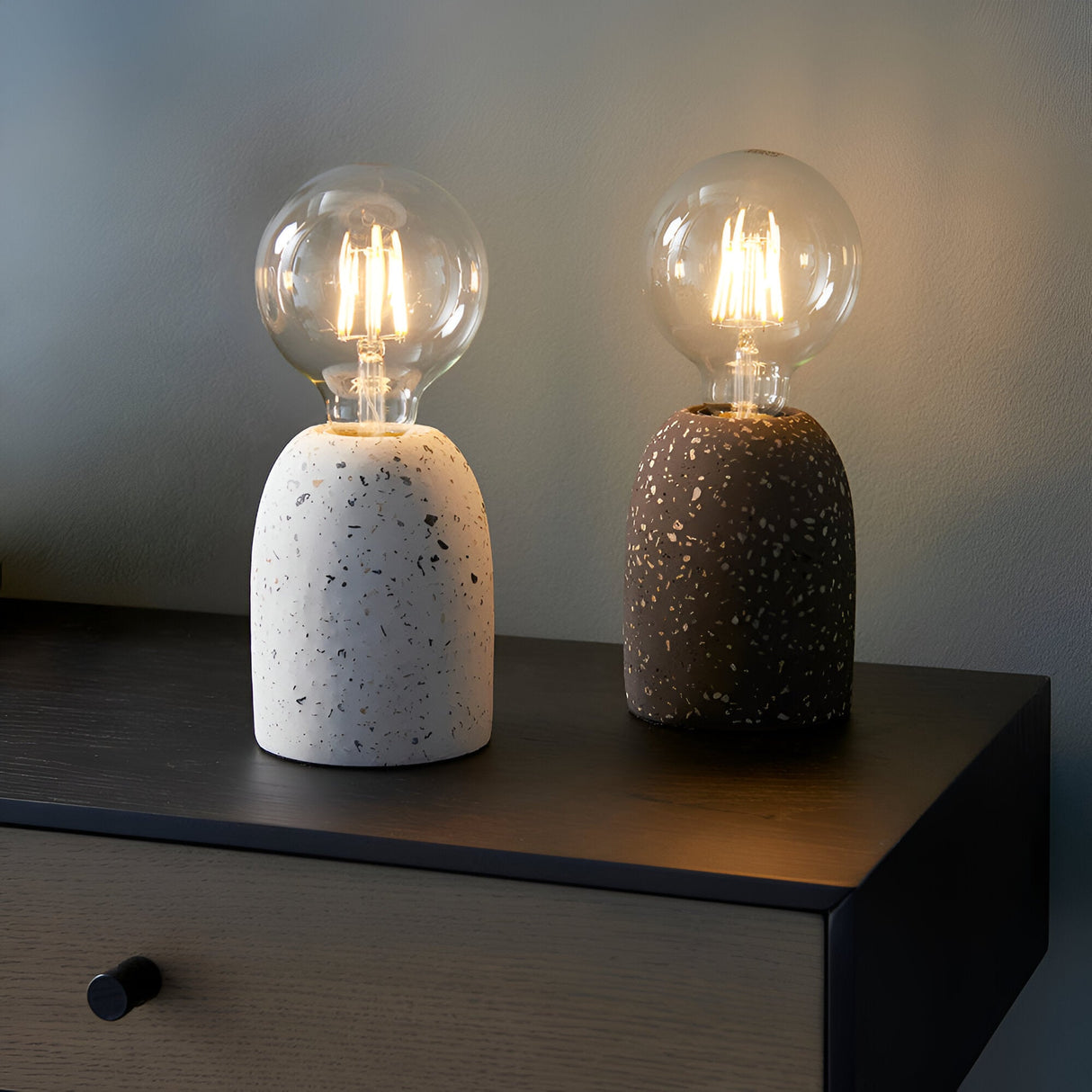 Endon Crangrove white terrazzo table lamps with speckled bases and exposed E27 filament globe bulbs, shown lit on a dark wood bedside drawer.