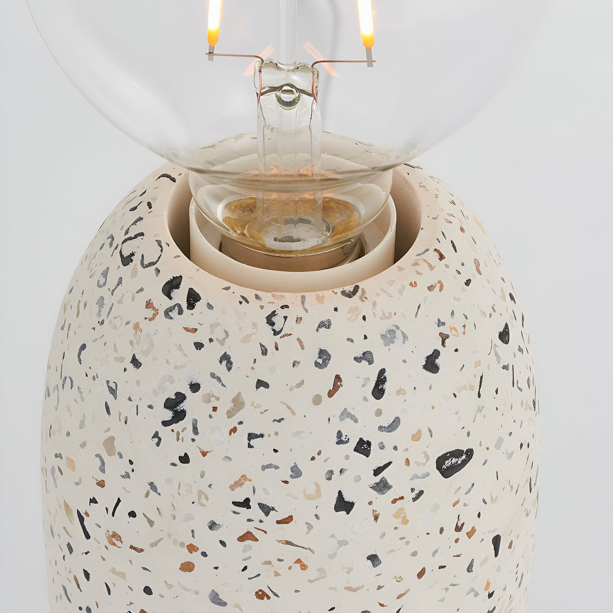 Close-up of the Endon Crangrove table lamp's white terrazzo base with black and brown speckles, showing the E27 fitting and clear filament globe bulb.