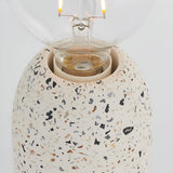 Close-up of the Endon Crangrove table lamp's white terrazzo base with black and brown speckles, showing the E27 fitting and clear filament globe bulb.