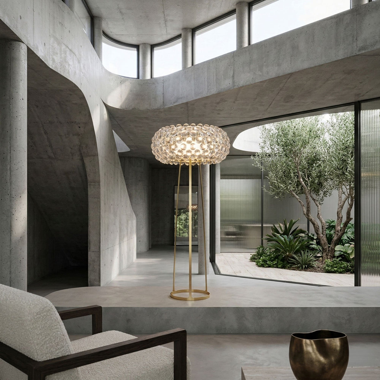 Briller LED Floor Lamp by Niori with clear acrylic sphere shade on a slim gold frame, in a concrete interior beside a boucle armchair and courtyard.
