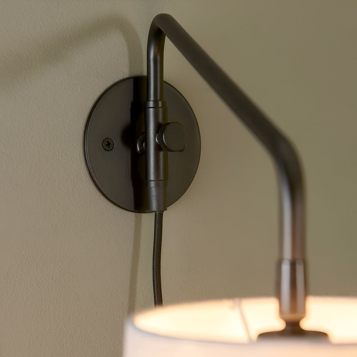 Close-up of the Endon Bevbourne plug-in wall light showing the matt black wall plate, adjustable swing arm and light grey fabric shade.