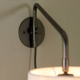 Close-up of the Endon Bevbourne plug-in wall light showing the matt black wall plate, adjustable swing arm and light grey fabric shade.