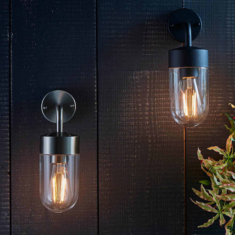 Endon Castfield outdoor wall lights in matt black and brushed steel, cylindrical clear glass casings with E27 filament bulbs, mounted on dark timber wall.