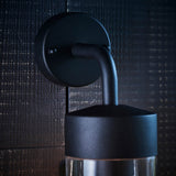 Endon Castfield outdoor wall light in matt black, close-up of the round wall plate and curved arm above the cylindrical shade with clear glass base.
