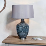 Endon Brenwick table lamp with black speckled glass body, matt nickel base and tapered mink shade on a wooden sideboard beside a round mirror and notebooks.