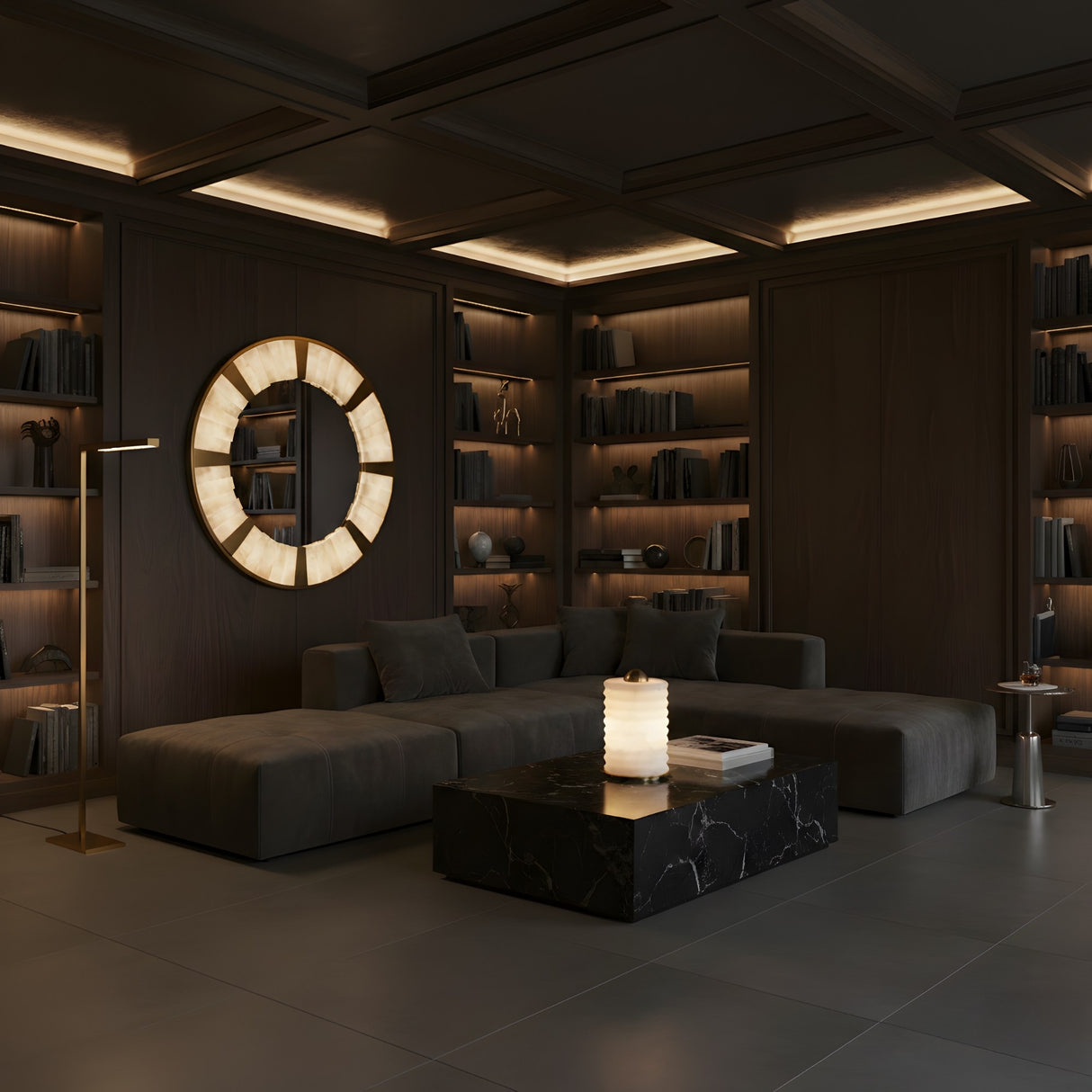 A modern, dimly lit living room with dark walls, built-in shelves, a large sectional, and a black marble coffee table features the Aurelior LED Small Ribbed Alabaster Table Lamp – Soft White glowing elegantly beneath a round backlit wall mirror.