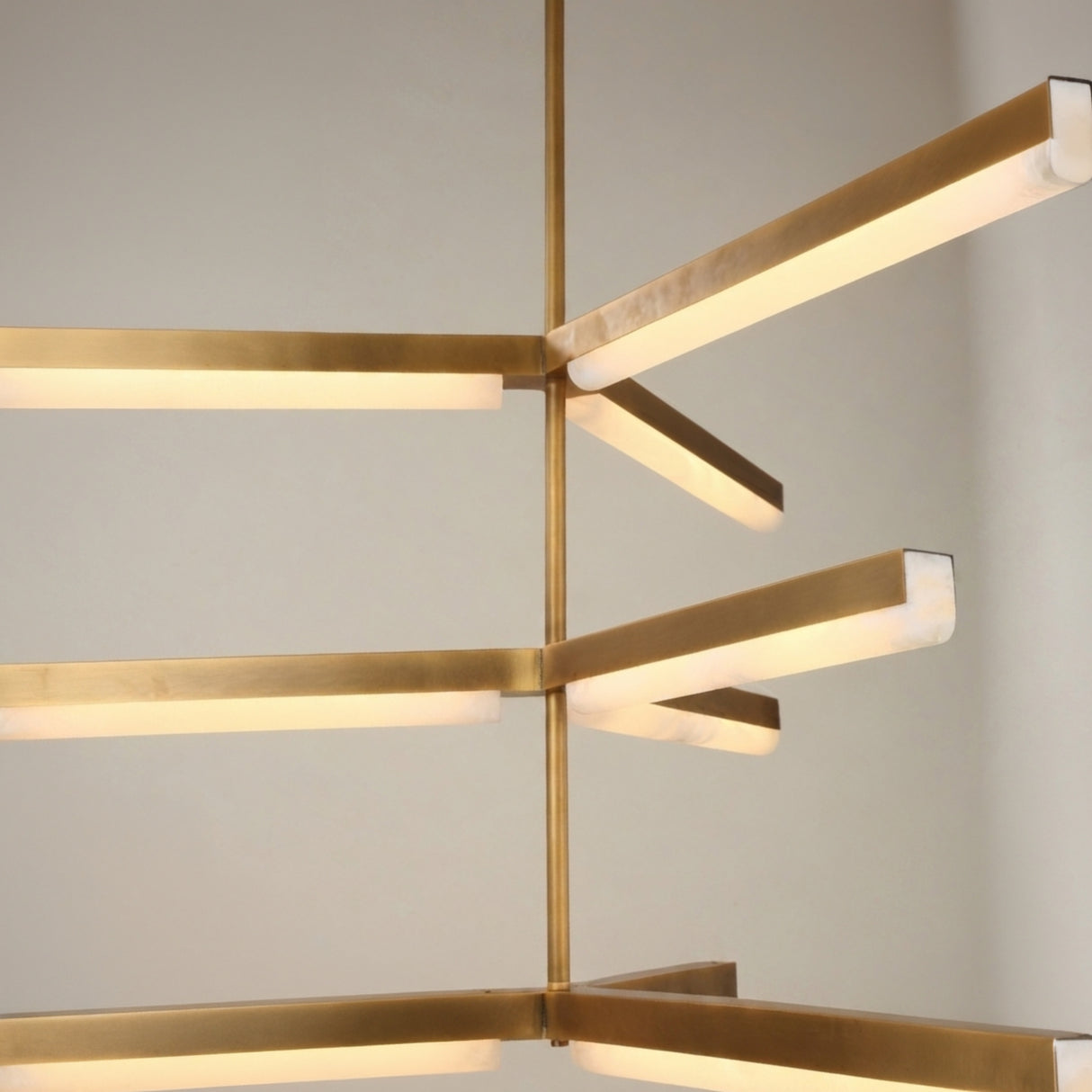 Close-up of the Elvaris 3-tier radial chandelier showing illuminated alabaster bars in a brushed brass frame with central rod, set against a plain light background.