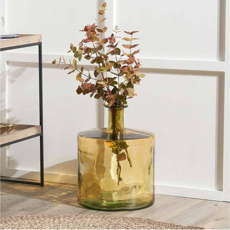 Amber recycled glass bottle vase, 45cm, with a wide rounded body and narrow neck, holding dried eucalyptus stems in a living room setting.