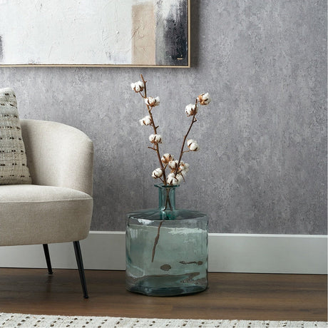 Clear recycled glass bottle vase, 45cm, with a wide rounded base and narrow neck holding cotton stems, shown beside a beige armchair on a wooden floor.