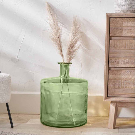 Forest Green Recycled Glass Bottle Vase, 45cm, with narrow neck holding pampas grass stems, shown on wooden flooring beside a wood drawer unit.
