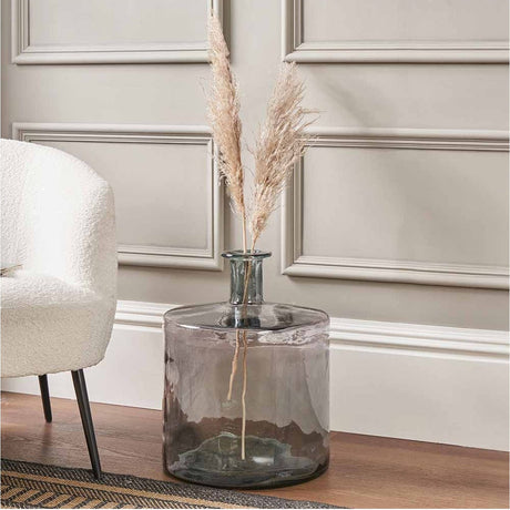 Grey recycled glass bottle vase, 45cm, with a wide rounded body and narrow neck, styled with pampas grass beside an armchair in a living room.