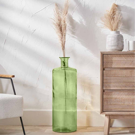 Tall forest green recycled glass bottle vase, 75cm, holding dried pampas grass, styled on a wooden floor beside an armchair and wooden drawer unit.