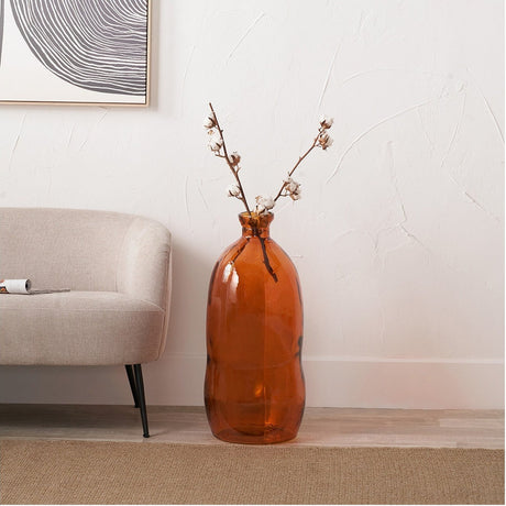 Orange Organic Shaped Recycled Glass Tall Vase, 73cm, with cotton stems, standing on the floor beside a beige armchair in a living room.