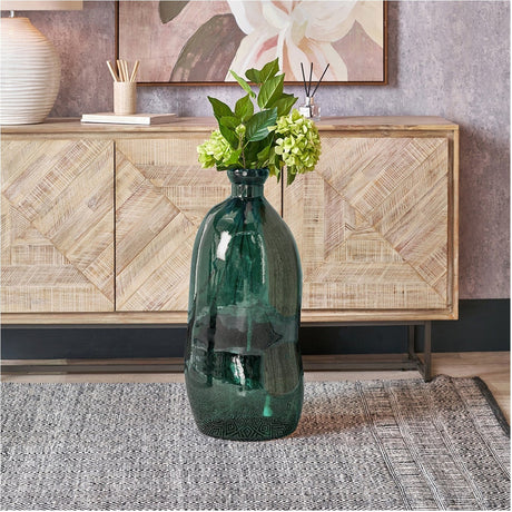 Sea Green Organic Shaped Recycled Glass Tall Vase, 73cm, holding leafy stems and green hydrangea, styled on a rug in front of a wooden sideboard.