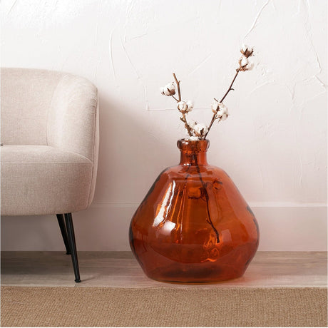 Orange Organic Shaped Recycled Glass Vase, 50cm, with a rounded bulbous glass body and narrow neck, holding cotton stems, styled beside a beige armchair.