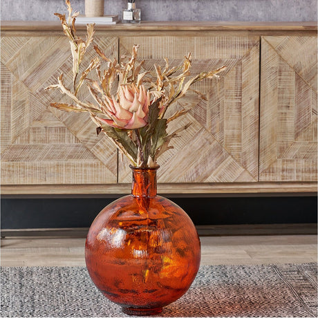 Orange recycled glass vase, 34cm, with a round textured body and narrow neck, holding dried foliage and a pink protea on a wooden sideboard.