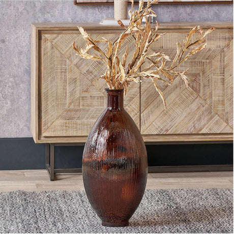 Pecan Brown Tall Recycled Ribbed Glass Vase, 29cm, holding dried foliage stems, styled on a rug in front of a wooden sideboard in a living room setting.