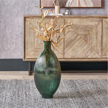 Sea Green Tall Recycled Ribbed Glass Vase with faux golden foliage, styled on a rug in front of a wooden sideboard in a living room setting.