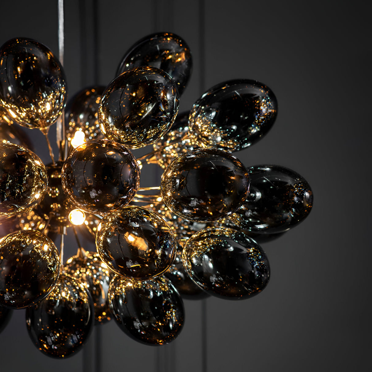 Close-up of Endon Brenworth 8 Light Pendant in black chrome with clustered electro-plated dark chrome glass shades glowing warmly against a grey wall.