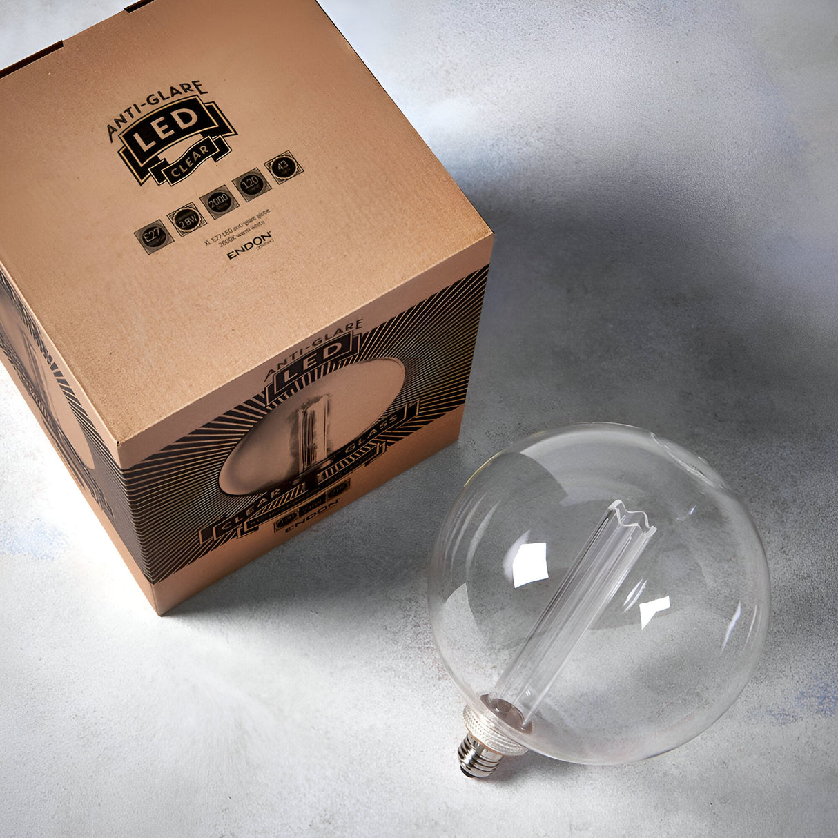 Endon 2.8W E27 LED clear globe bulb with internal etched diffuser sleeve, shown beside its printed kraft packaging on a light grey surface.