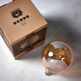 Endon 2.8W E27 LED amber globe bulb beside its printed kraft box on a light grey surface.