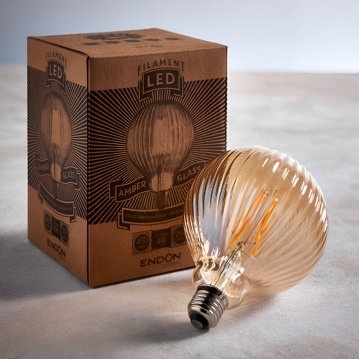 4W E27 LED Filament Ribb Bulb in amber glass with visible glowing filament and screw cap, shown beside its Filament LED packaging box.