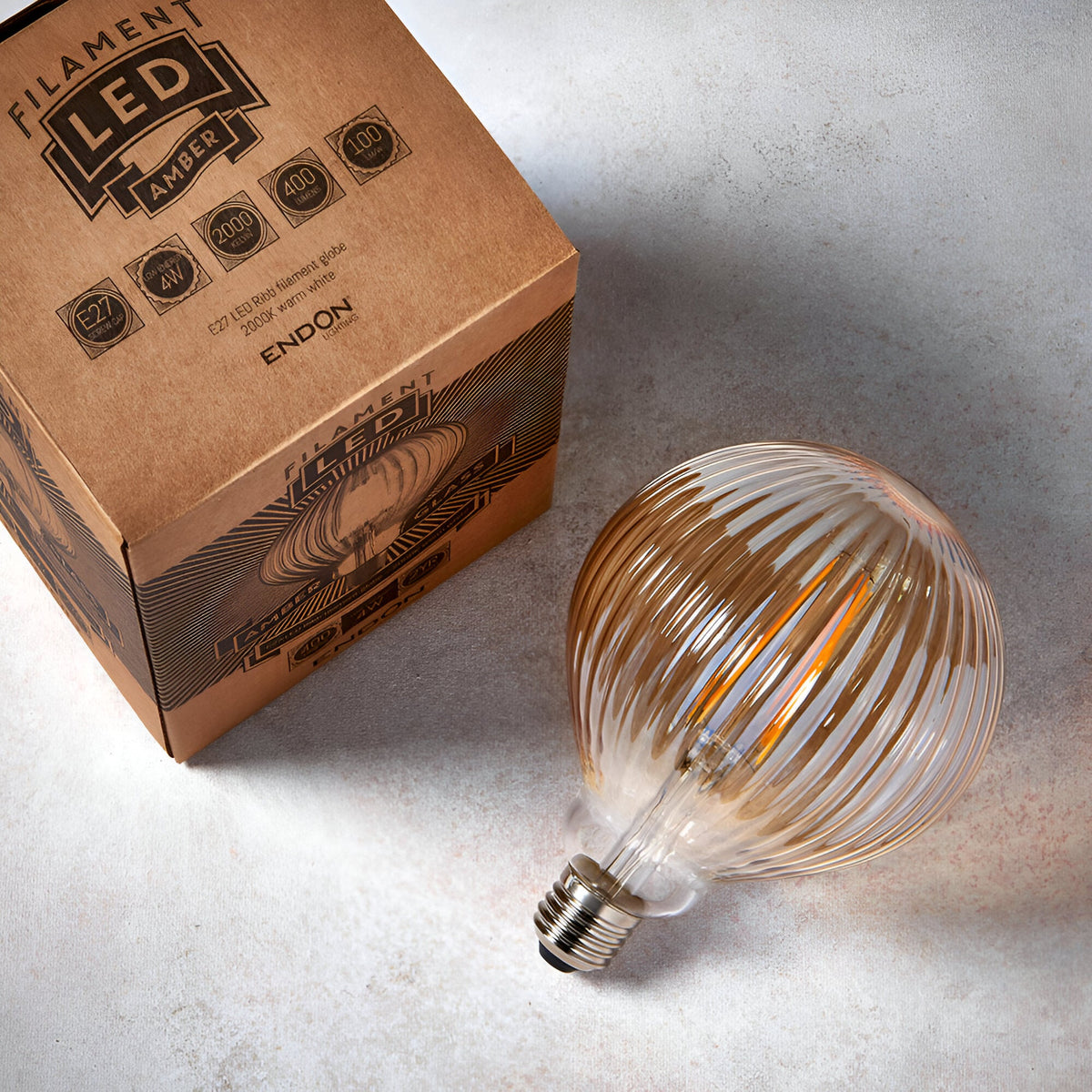 4W E27 LED Filament Ribb Bulb in amber tinted ribbed glass with visible warm white filament, E27 screw cap, shown beside its Filament LED packaging.