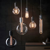 Endon E27 LED filament pear bulbs shown as pendant lights in varied clear and ribbed glass shapes, glowing warm white against a dark slate wall.
