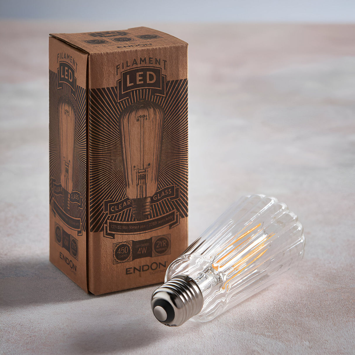 Endon 4W E27 LED filament pear bulb with ribbed clear glass lying beside its printed kraft box on a neutral background.