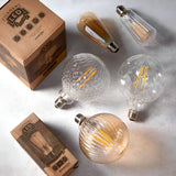 Endon 4W E27 LED filament bulbs in pear, teardrop, ribbed globe and faceted globe shapes with clear and amber glass, shown beside kraft product boxes.