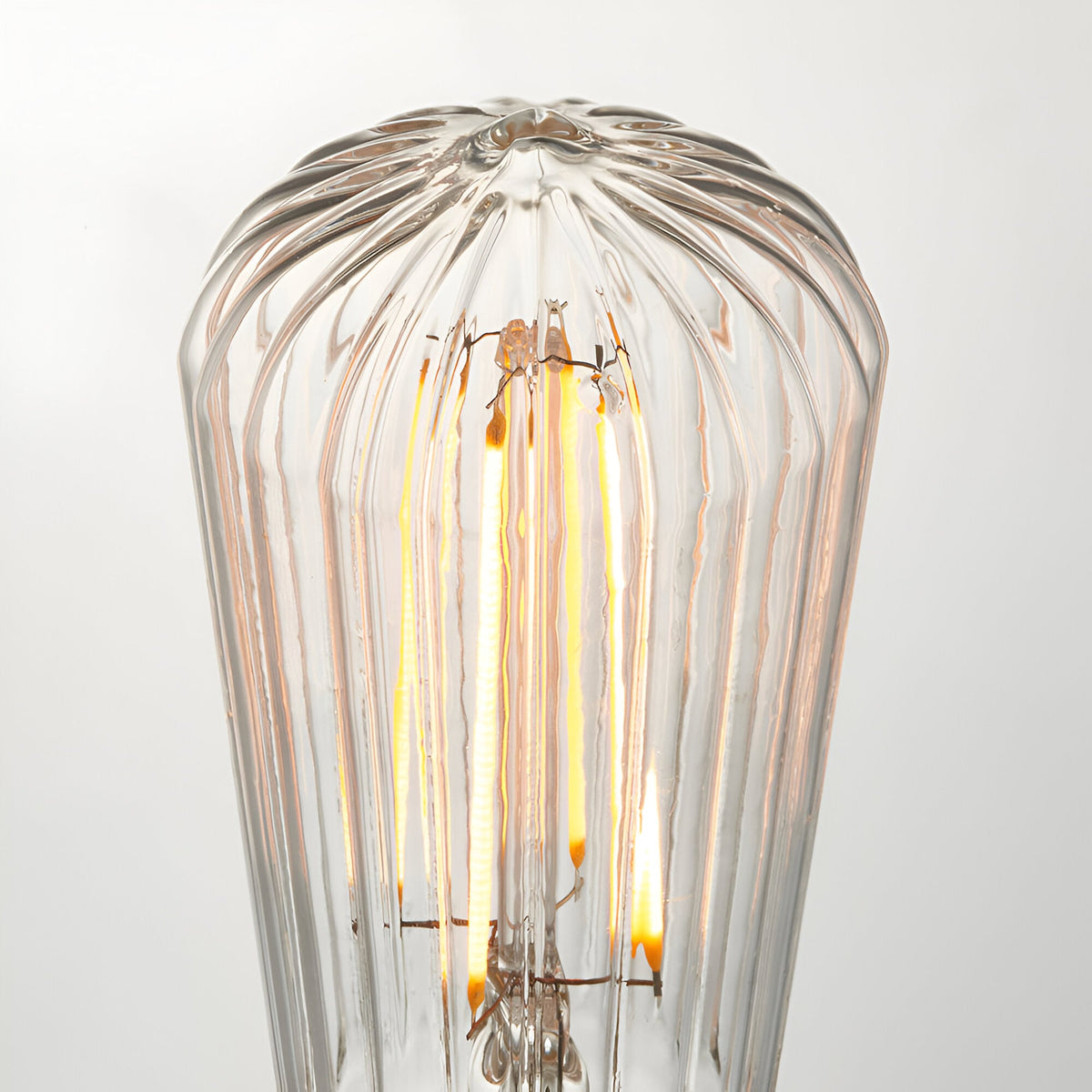 Close-up of Endon 4W E27 LED filament pear bulb in clear ribbed glass, glowing warm white against a plain light background.