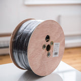 AVSL Mercury 100V line speaker cable 1.15mm² in black on a wooden 100m reel, spec label visible on the flat side, shown on a white surface.