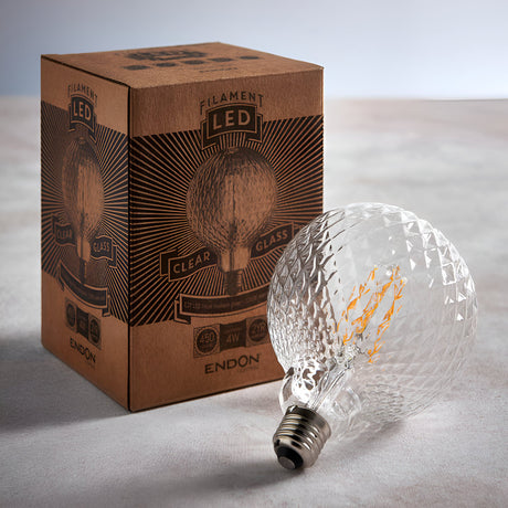 Endon 4W E27 LED filament faceted globe bulb in clear glass with metal screw base, resting beside its brown printed box on a neutral surface.