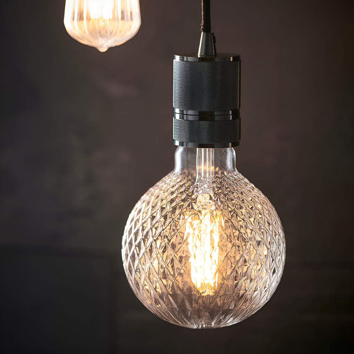 Endon 4W E27 LED filament faceted globe bulb in clear glass with warm white glow, suspended from a knurled matte black pendant fitting.