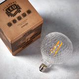 Endon 4W E27 LED filament facet globe bulb in clear faceted glass beside its printed kraft box on a pale grey surface.