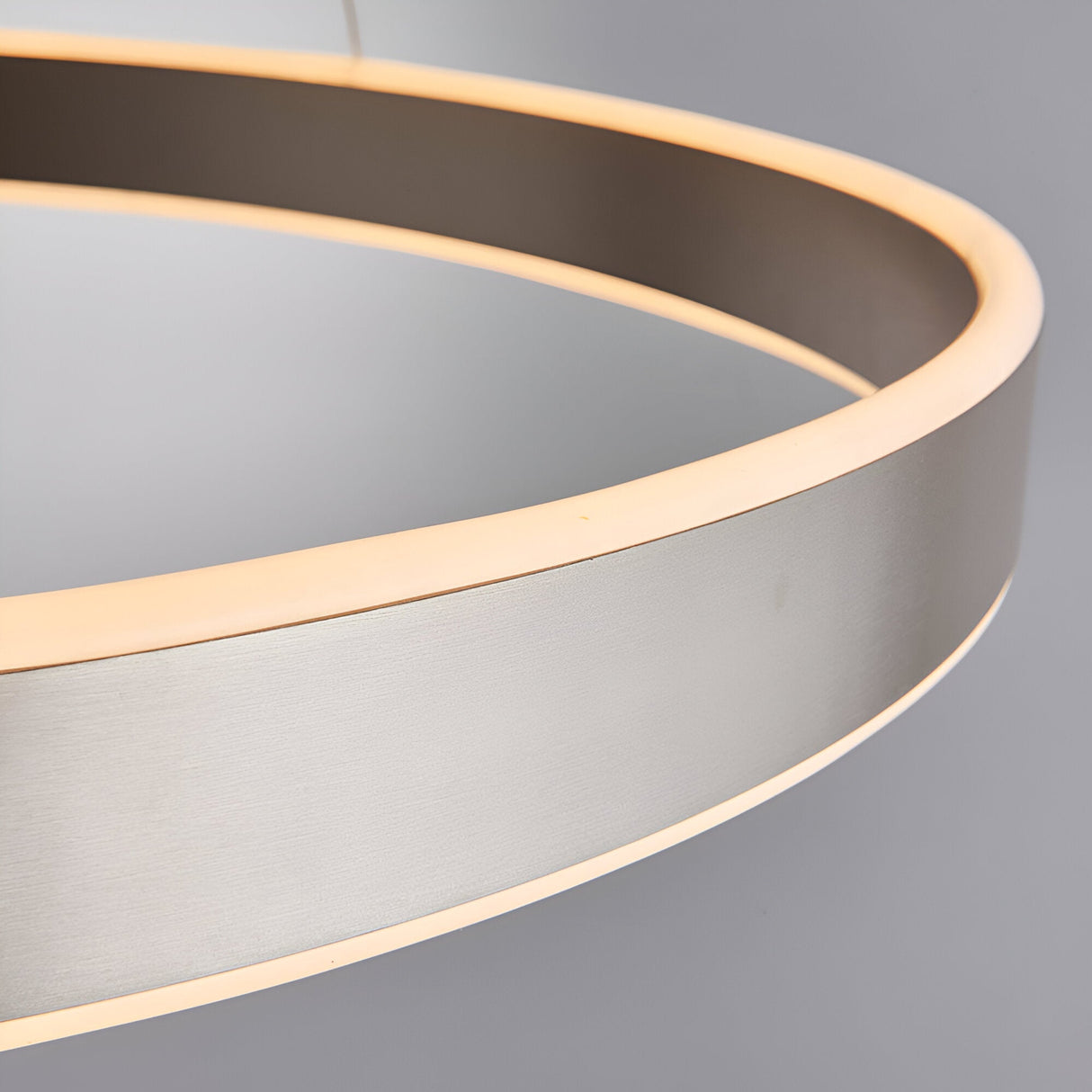 Close-up of the Bramford Pendant in matt nickel, a circular ring-shaped LED fixture with a frosted diffuser glowing warm white, against a plain grey background.