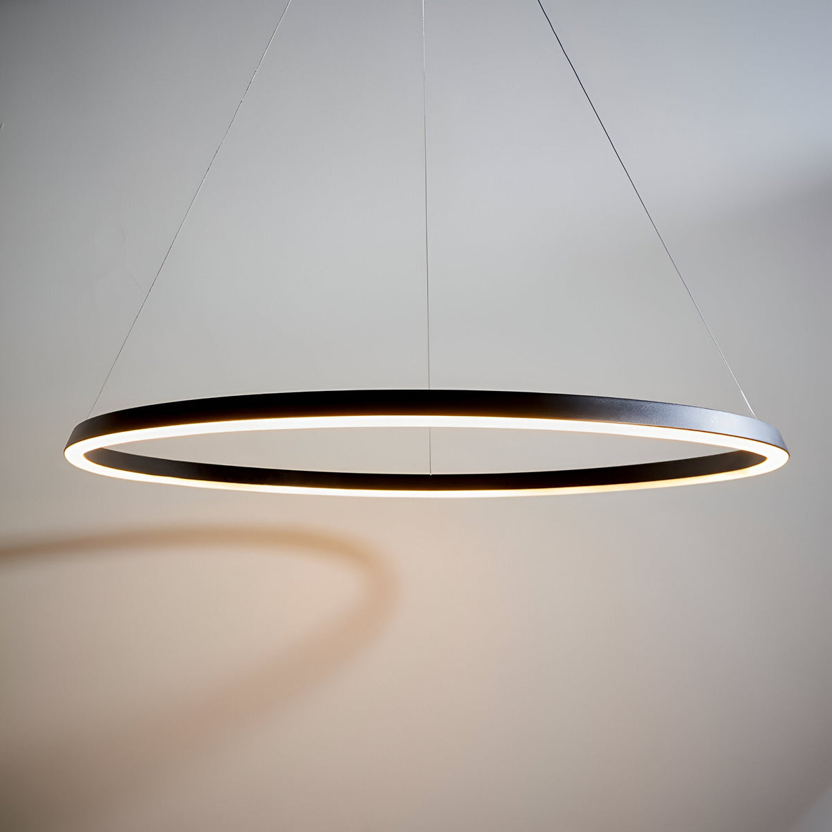 Cliffton LED Pendant in matte black, a large circular ring fixture with warm white diffused light, suspended by fine wire cables.