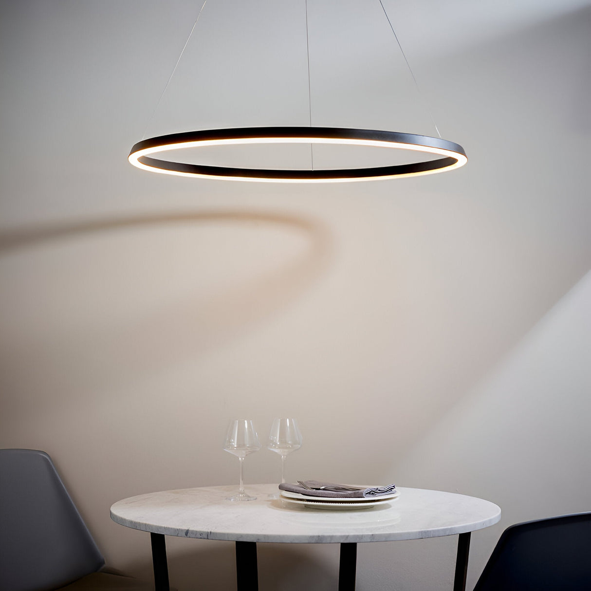 Cliffton LED pendant light in black, a large circular ring fixture with white diffuser glow, suspended above a marble dining table.
