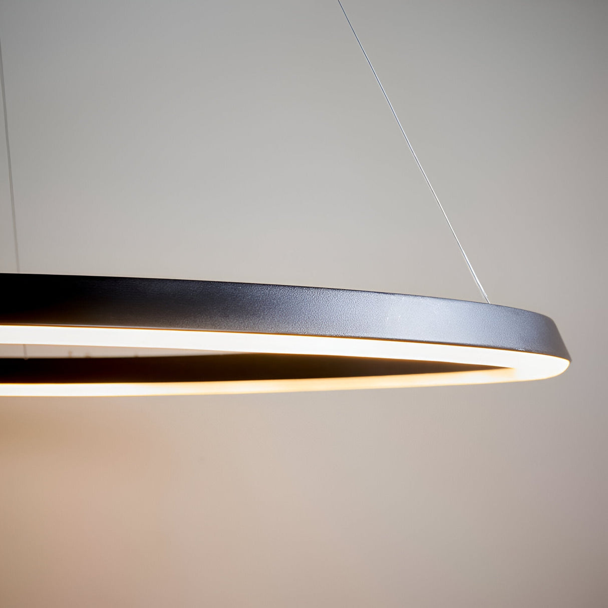 Cliffton LED pendant close-up showing slim black and white ring profile with warm diffused light, suspended by fine wire on a plain grey background.