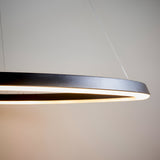 Cliffton LED pendant close-up showing slim black and white ring profile with warm diffused light, suspended by fine wire on a plain grey background.