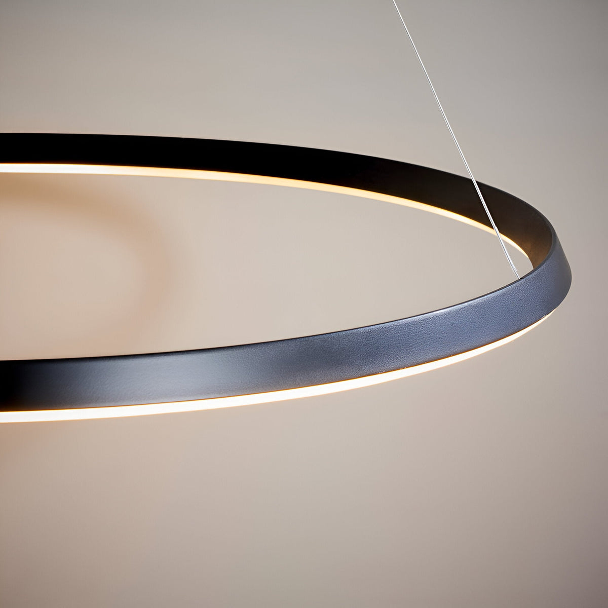 Close-up of the Cliffton LED pendant light, a black metal ring with an integrated white diffuser, suspended on wire cables against a neutral background.