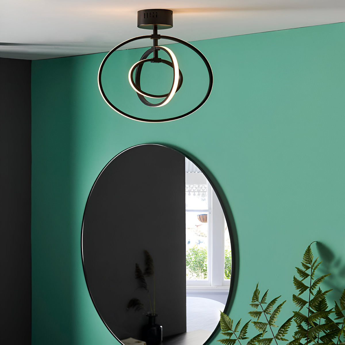 Endon Corso matt black semi-flush LED ceiling light with interlinked circular rings, fitted to a white ceiling above an oval mirror on a green wall.