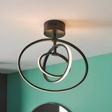 Endon Corso semi-flush ceiling light in matt black, with three interlocking LED rings, mounted on a green and white wall interior.